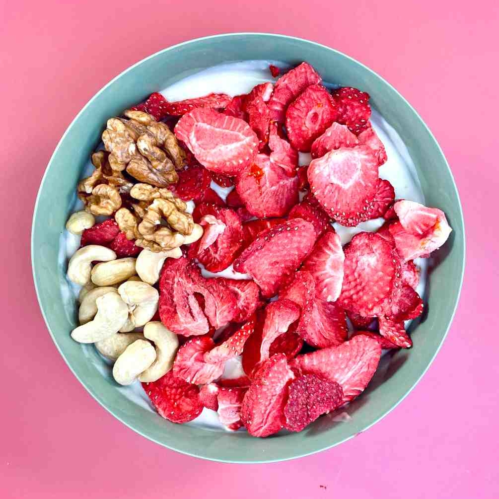 Gefriergetrocknete Erdbeeren in einer Müslischüssel mit Cashews, Walnüssen und Jogurth.